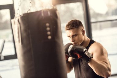 atletik genç adam boks kum torbası içinde jimnastik salonu ile eğitim eldiven