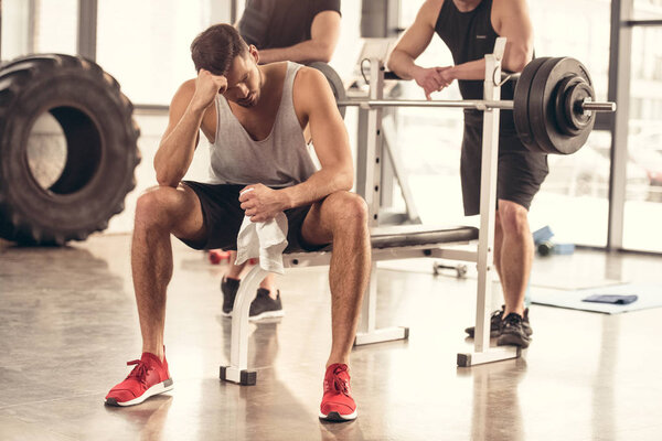 handsome tired sportsman sitting and resting on bench press in gym