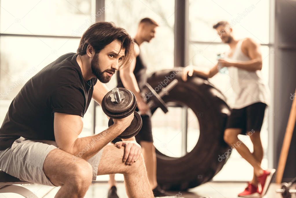 side view of handsome young man lifting dumbbell and looking away in gym 