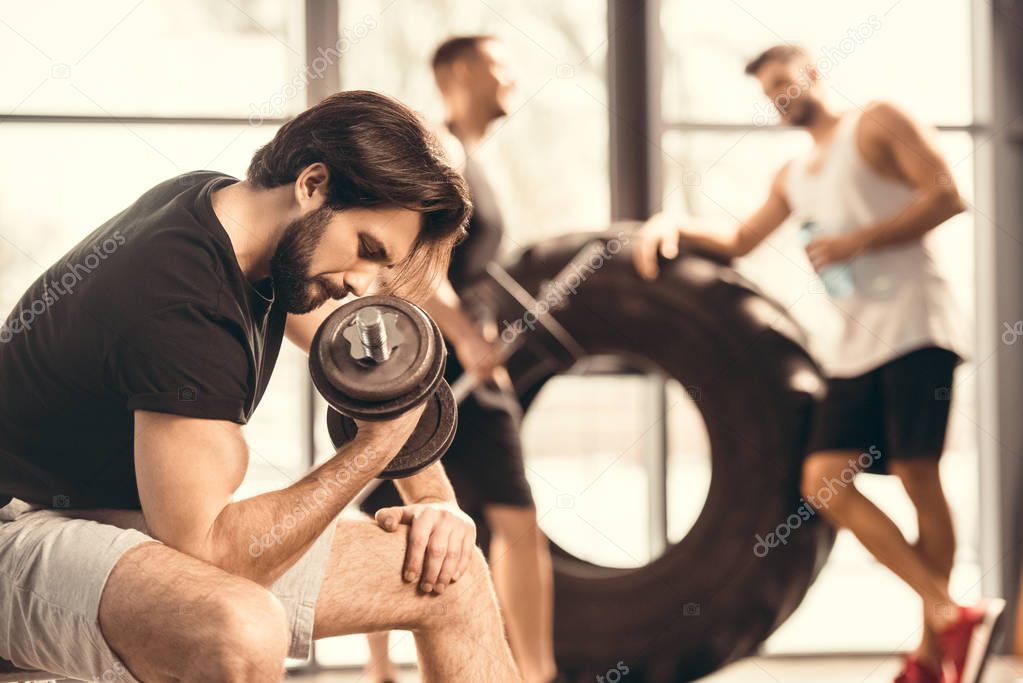 side view of muscular young man lifting dumbbell in gym 