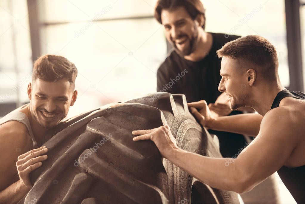 cheerful athletic young men training with tyre in gym