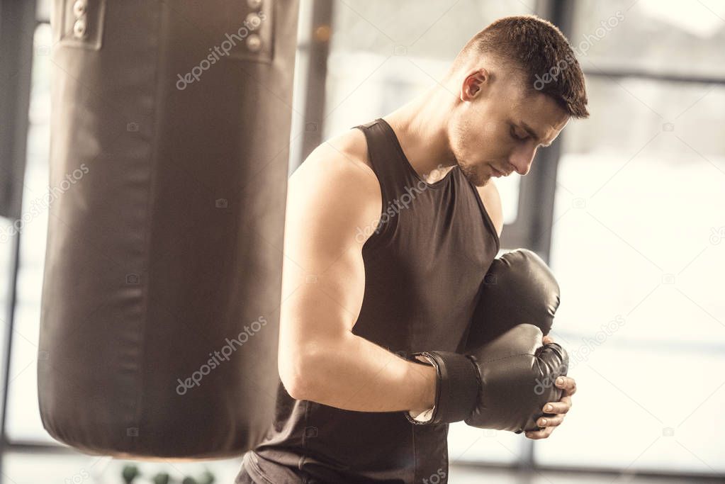 side view of muscular sportsman wearing boxing gloves in gym