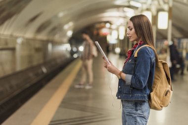 kulaklık ve metro istasyonunda dijital tablet ile şık kadın yan görünüm 