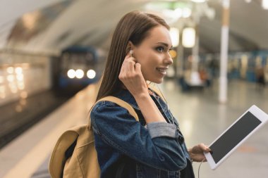 kulaklık ve metro istasyonunda dijital tablet ile gülümseyen genç kadın yan görünüm 
