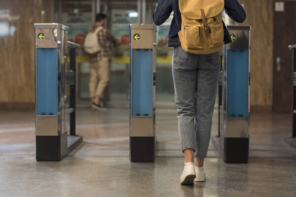 cropped shot of female stylish traveler with backpack passing through turnstiles and male tourist behind