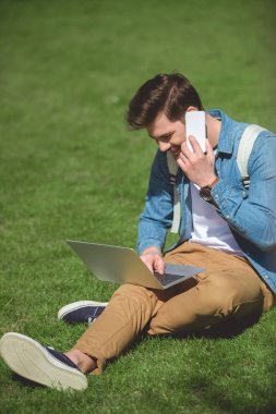 şık adam smartphone üzerinde konuşmak ve dizüstü çimenlerin üzerinde kullanma