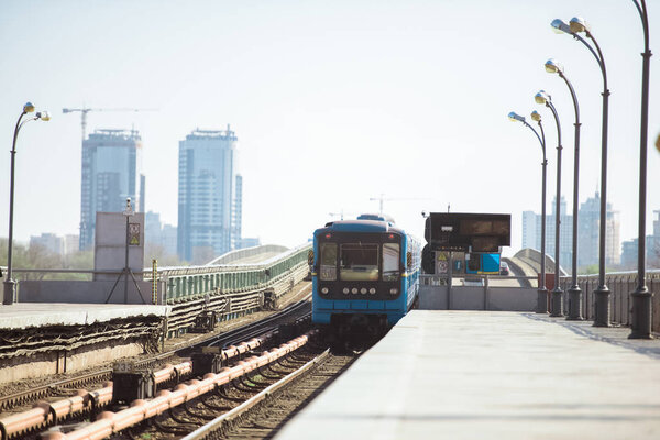 arriving train at outdoor subway station with buildings on background