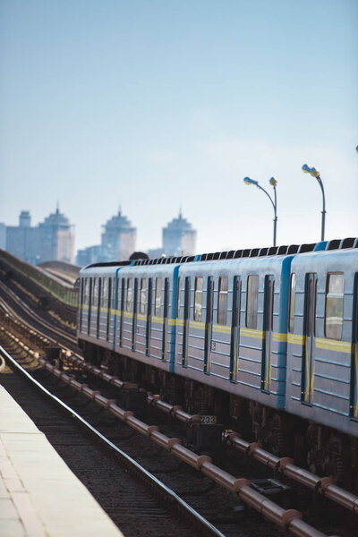 front view of train at outdoor subway station with buildings on background