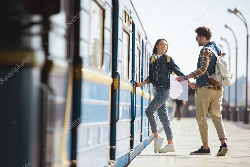 couple of stylish tourists with backpacks and map going into train at outdoor metro station 