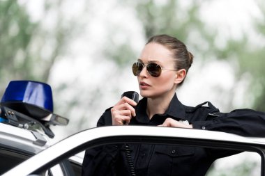 attractive policewoman talking by radio set near police car clipart
