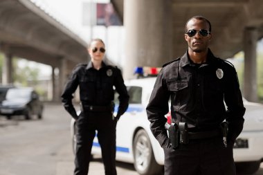 police officers with hands in pockets looking at camera in front of car clipart