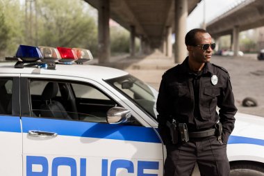african american police officer leaning back on car and looking away clipart