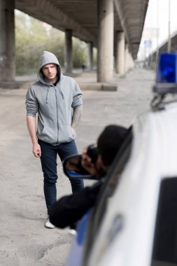 policeman looking on hooded young man on street out of window clipart