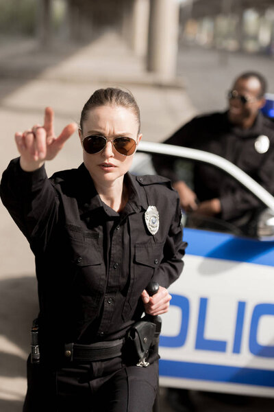 young serious policewoman pointing somewhere while her partner standing near car blurred on background