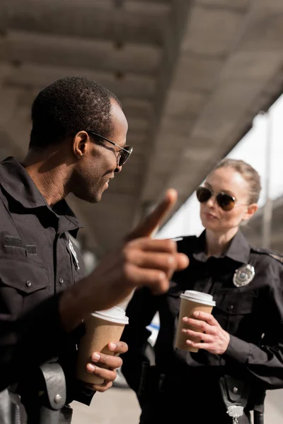 Policía Señalando Algún Lugar Mientras Bebe Café Para Con Pareja — Foto de stock gratis