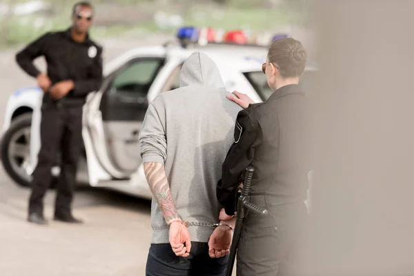 Visão Traseira Policial Prendendo Criminoso Masculino Algemado Enquanto Parceiro Atrás — Fotografia de Stock