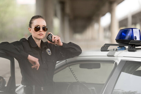 policewoman in sunglasses talking on portable radio near car 