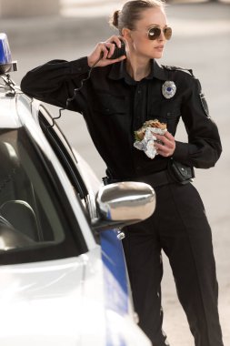 Burger holding ve radyo sette konuşan genç polis 