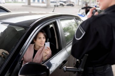 policewoman with portable radio and young woman in car holding driver license clipart