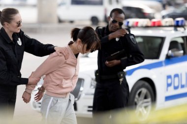 policewoman holding arrested young woman while her partner talking on portable radio   clipart