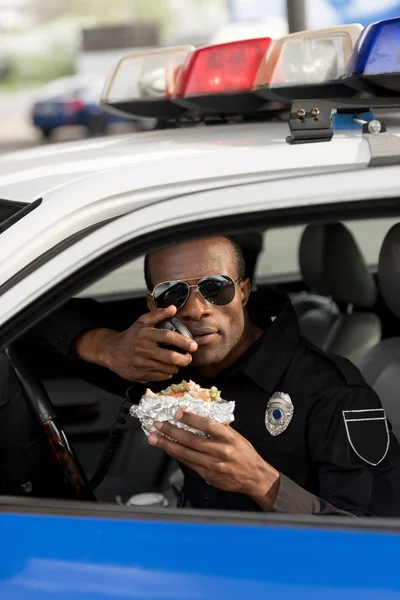 Americký Policista Drží Burger Mluví Přenosné Rádio Autě — Stock fotografie zdarma