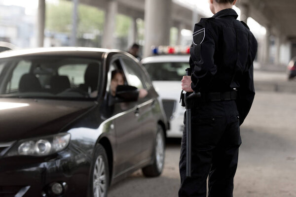 cropped shot of policewoman holding truncheon and stopped car 