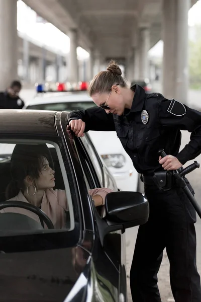 Vista Lateral Mujer Policía Sosteniendo Porra Hablando Con Joven Sentada —  Fotos de Stock