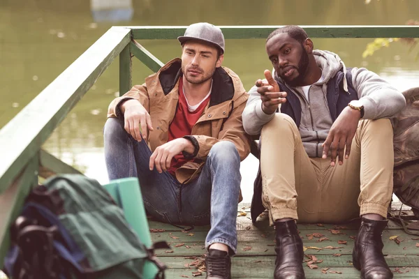 Junge Männer mit Rucksäcken sitzen auf Seebrücke — Stockfoto