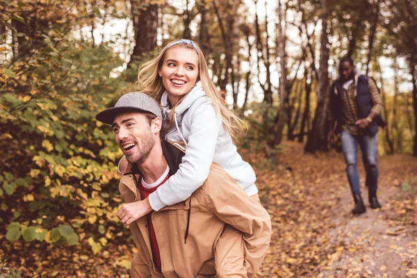 Feliz joven pareja piggybacking en bosque - foto de stock