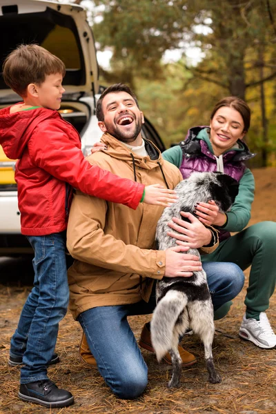 Famille heureuse jouant avec le chien dans la forêt — Photo de stock