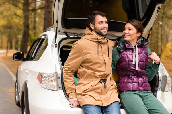 Pareja sonriente sentada en el maletero - foto de stock