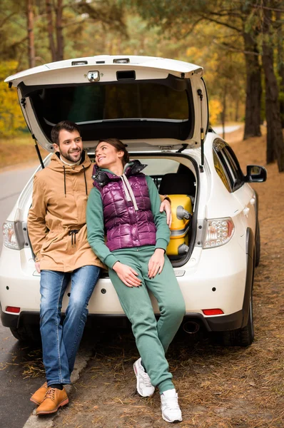 Pareja sonriente sentada en el maletero - foto de stock