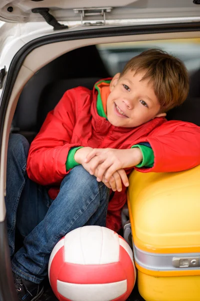 Smiling boy sitting in car trunk — Stock Photo