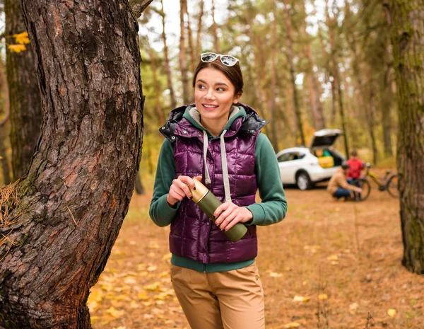 Lächelnde Frau mit Thermoskanne im Herbstwald — Stockfoto