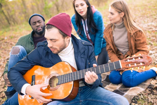 Друзья наслаждаются гитарой в осеннем парке — стоковое фото