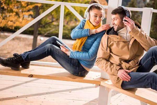 Pareja joven sentada en el banco en auriculares - foto de stock