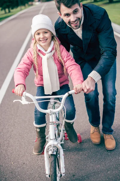 Отец учит дочь кататься на велосипеде — стоковое фото