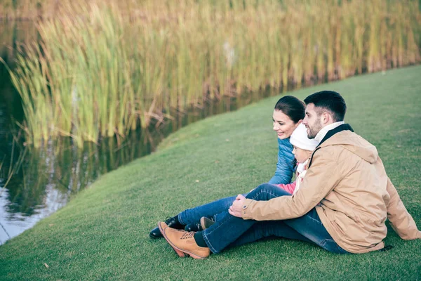 Famiglia sorridente seduta vicino al lago — Foto stock