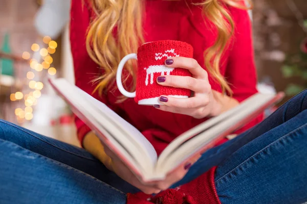 Woman reading book with hot drink — Stock Photo