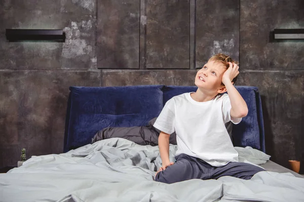 Задумчивый мальчик сидит на кровати — стоковое фото