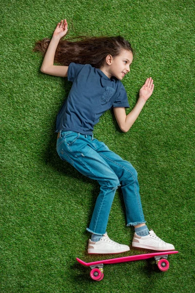 Chica con monopatín acostado en la hierba - foto de stock