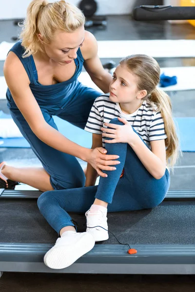 Woman helping girl injured knee sitting on treadmill — Stock Photo