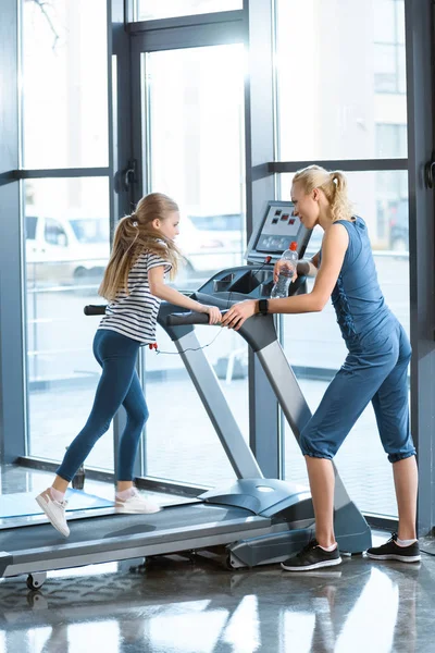 Woman trainer looking at small girl workout on treadmill — Stock Photo