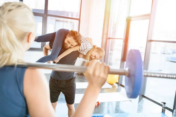 Woman workout with barbell while man having fun with daughter on his shoulders — Stock Photo