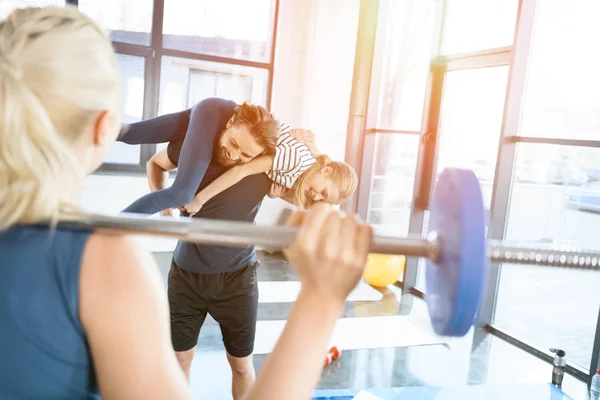 Entrenamiento de mujer con barra de pesas mientras el hombre se divierte con la hija sobre sus hombros - foto de stock