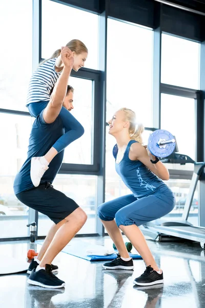 Woman workout with barbell while man having fun with daughter on his shoulders — Stock Photo