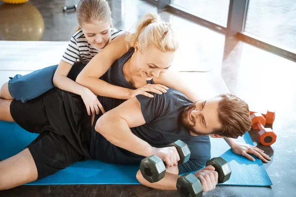 Famille heureuse s'amuser à la salle de gym, homme tenant haltères — Photo de stock