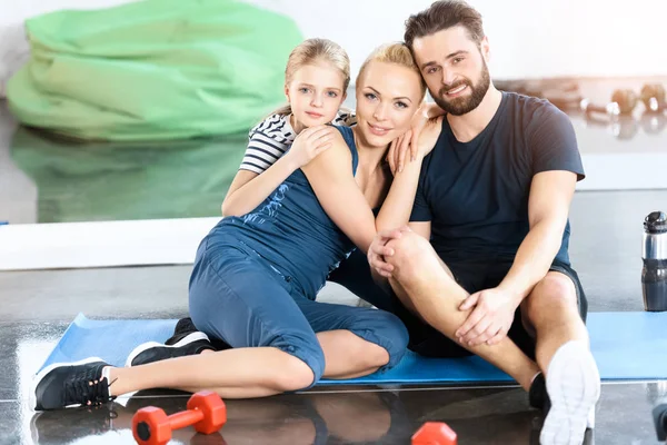 Retrato de la familia feliz sentado en la estera en el gimnasio - foto de stock