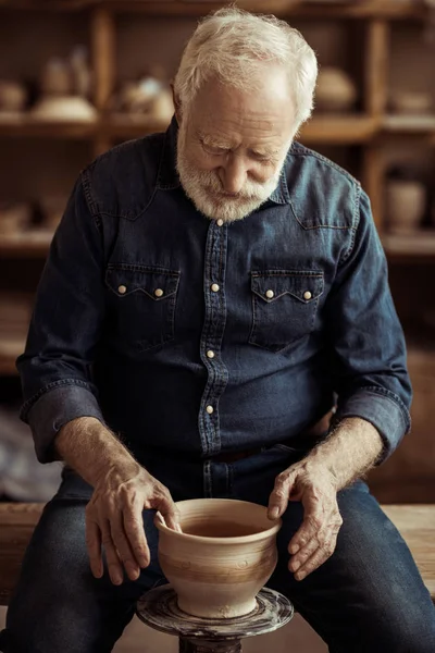 Alfarero mayor haciendo cerámica en una rueda en el taller - foto de stock