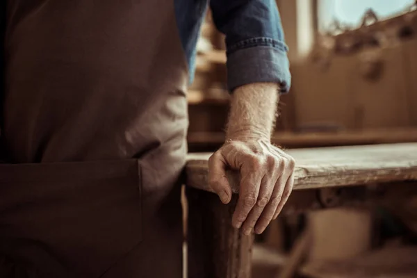 Abgeschnittenes Bild eines Töpfers, der in der Werkstatt auf einem Tisch steht und lehnt — Stockfoto
